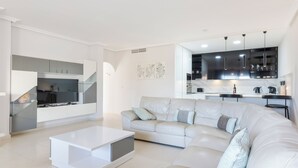 Una sala de estar moderna con un sofá seccional blanco, una mesa de centro blanca y una cocina al fondo.