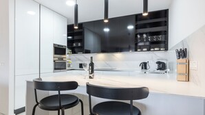 Una cocina moderna con armarios blancos, encimera de mármol, dos taburetes negros y un salpicadero negro.