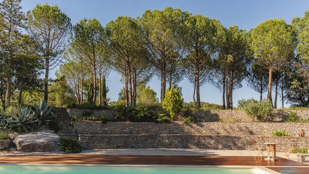 Un espace piscine doté d’une terrasse en bois, d’escaliers en pierre et entouré d’arbres.