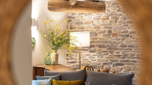 Un salon chaleureux avec un mur en pierre, une poutre en bois au plafond et un canapé bleu agrémenté de coussins.