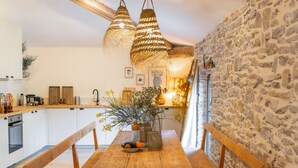 Une table à manger en bois avec des bancs, un mur en pierre et des luminaires suspendus dans un coin cuisine.