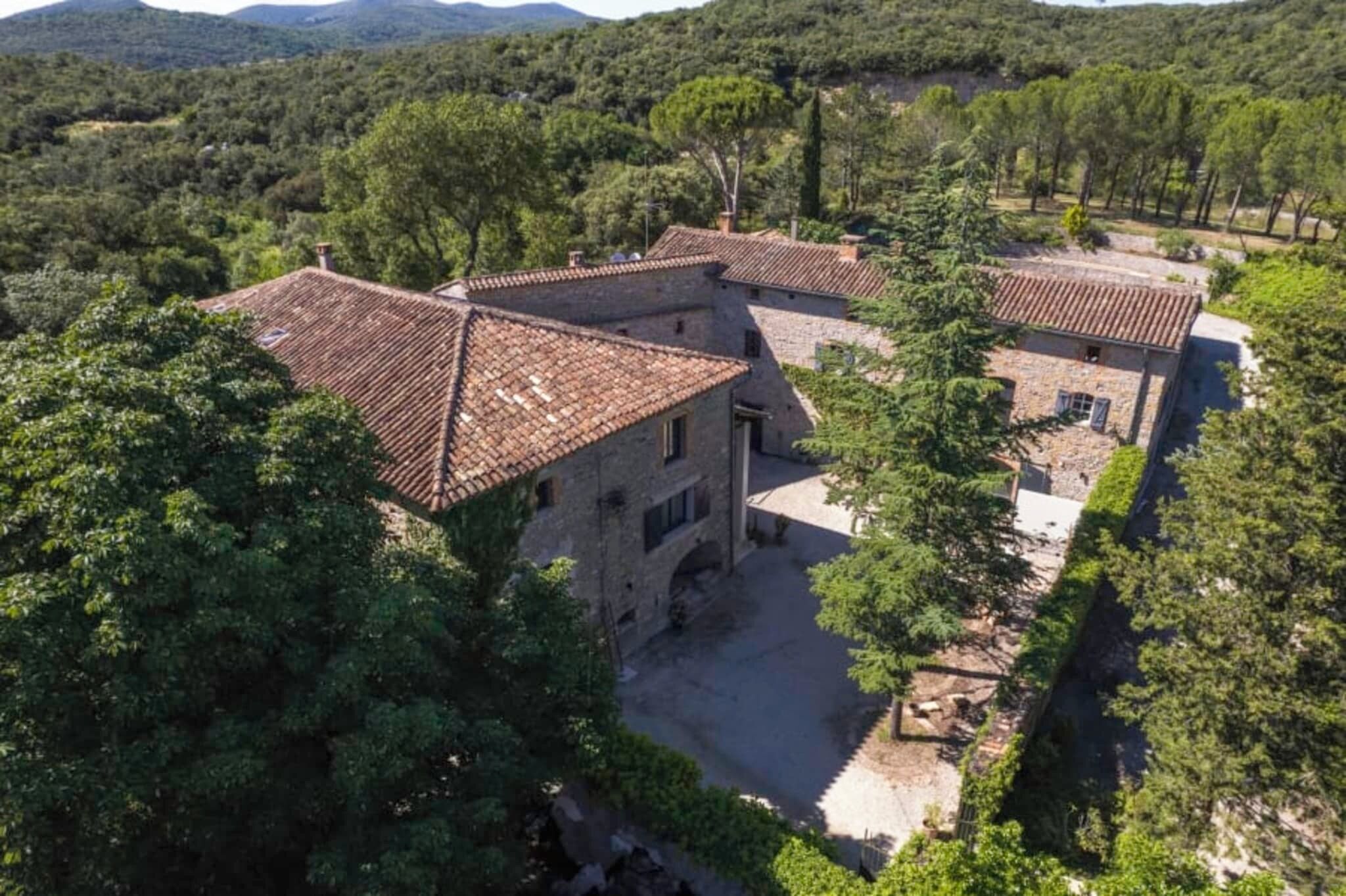 Un bâtiment en pierre, doté d’un toit en tuiles, entouré d’arbres et situé dans un paysage vallonné.