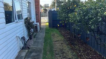 Un jardin à l’arrière d’une maison, avec une maison blanche, une terrasse en bois, un parterre fleuri et une clôture.