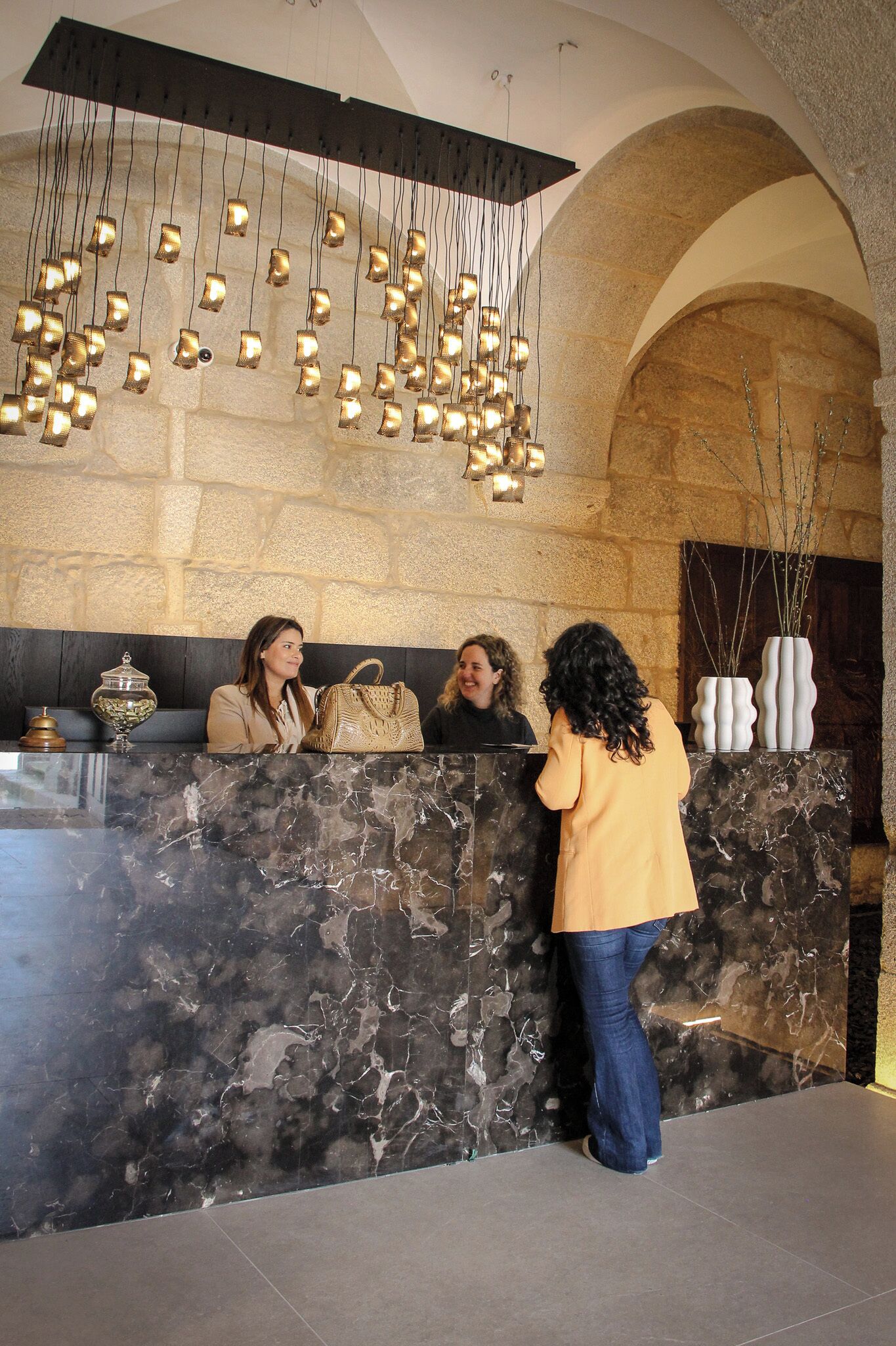 Un área de recepción con mostrador de mármol, lámparas colgantes y pared de piedra.