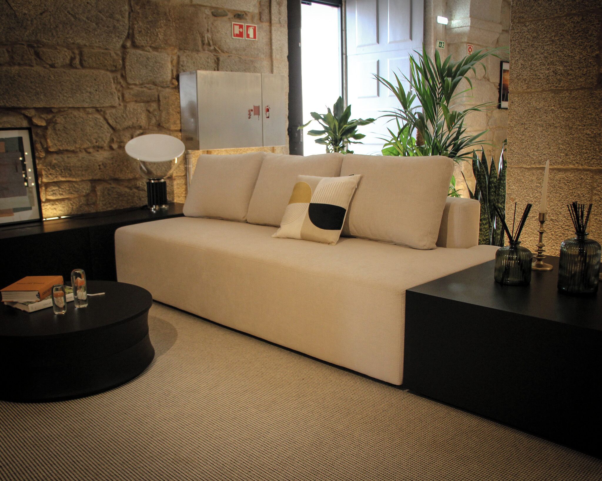 Un salon moderne avec un canapé beige, une table basse ronde noire et une table d’appoint agrémentée d’objets décoratifs.