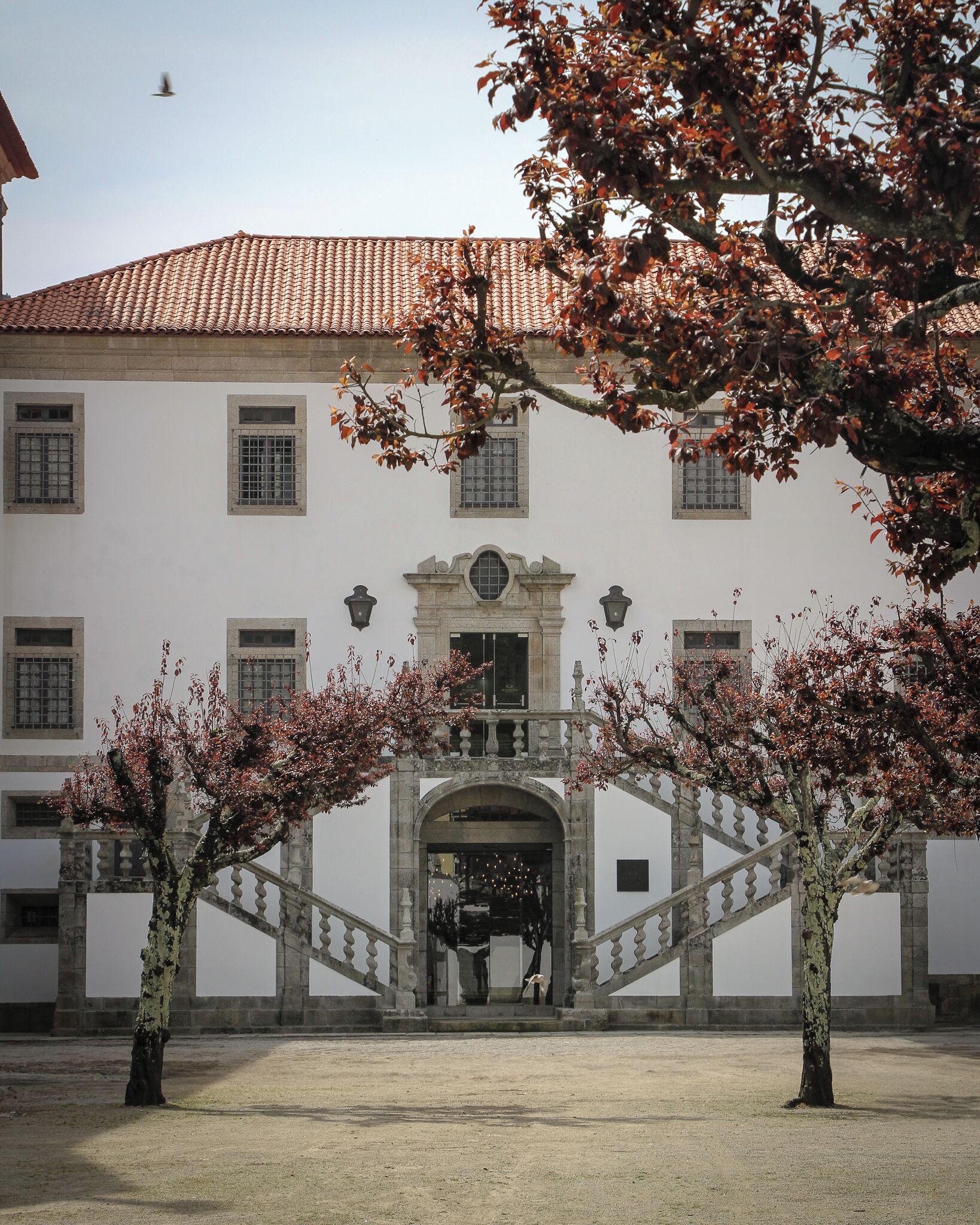 Un edificio storico con tetto in tegole, un arco centrale e un cortile alberato.