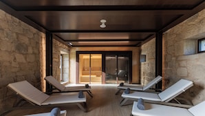 A spa area with four sun loungers, a wooden ceiling, stone walls, and a large sliding glass door leading to an outdoor area. - MS Collection Arouca Mosteiro de Arouca (Arouca)