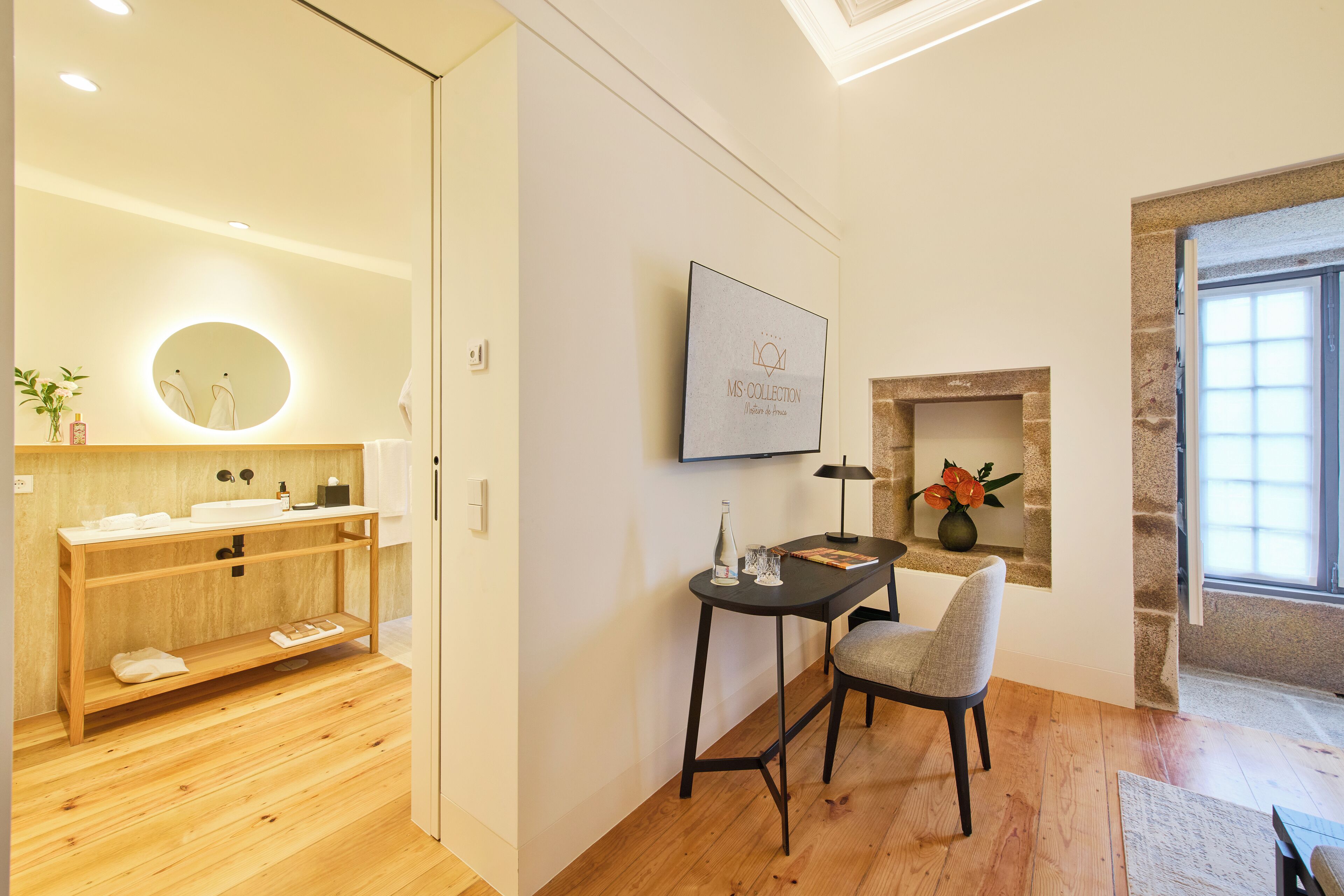 A modern bathroom with a wooden vanity, a round mirror, and a small table with a chair.