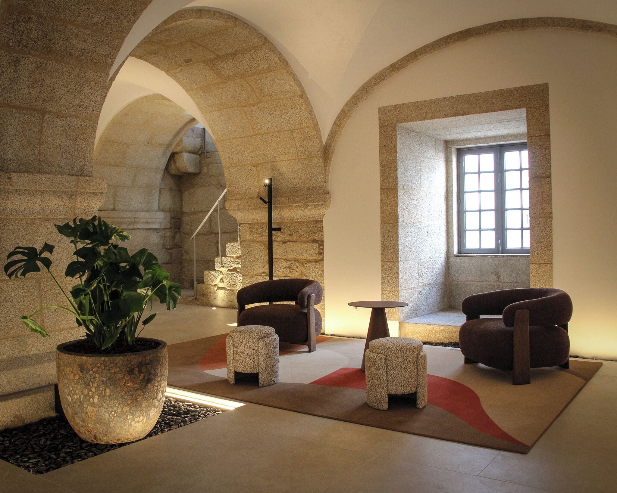 A modern interior with stone arches, a large potted plant, and two leather sofas.