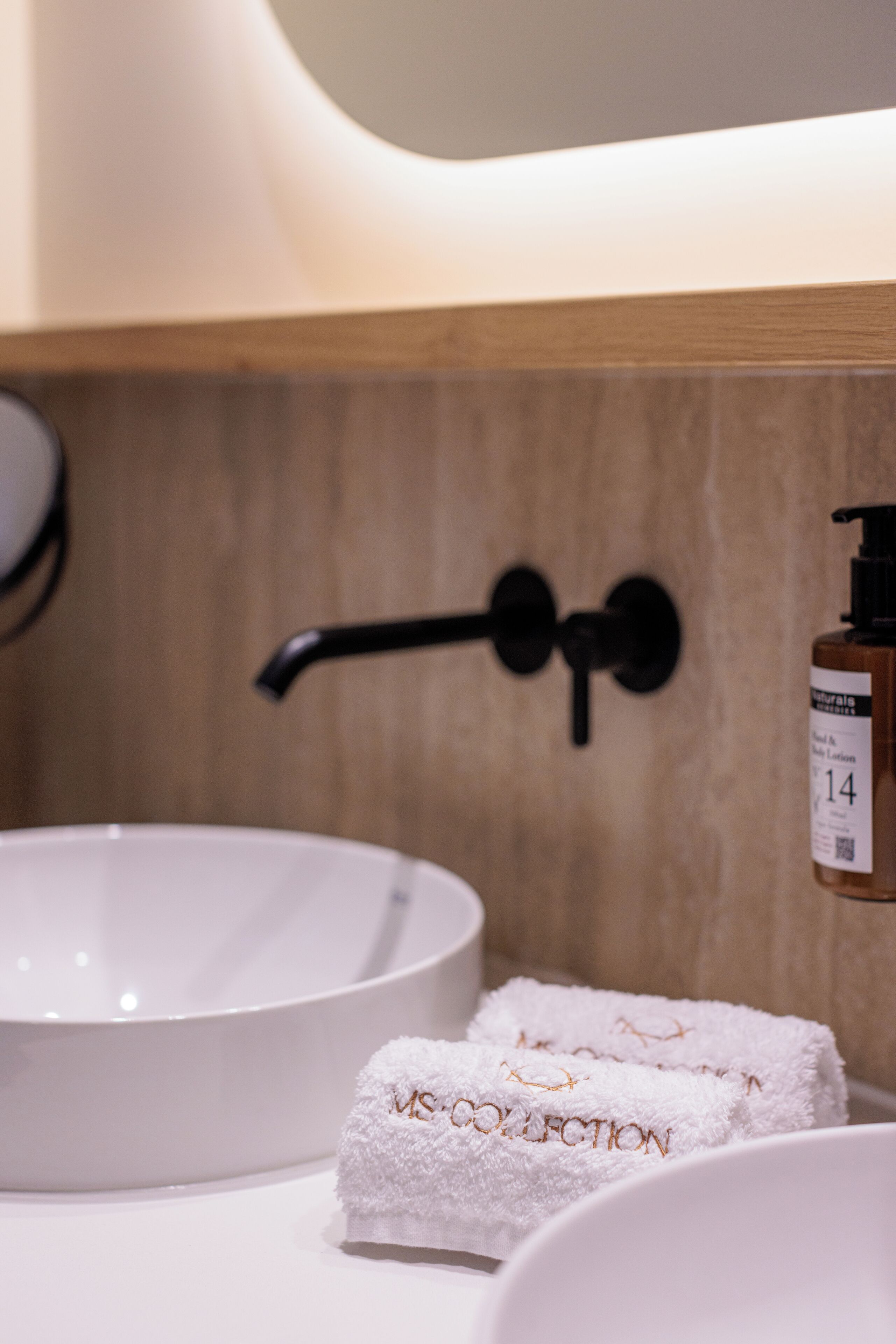 Een badkamer met een witte wastafel, een zwarte kraan en een fles shampoo.