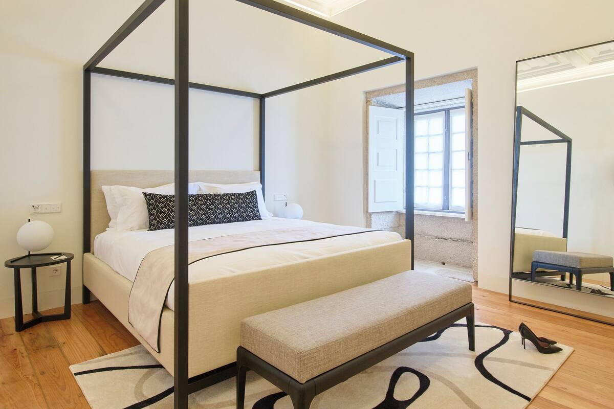 A four-poster bed with a bench, a bedside table, and a mirror on the wall.