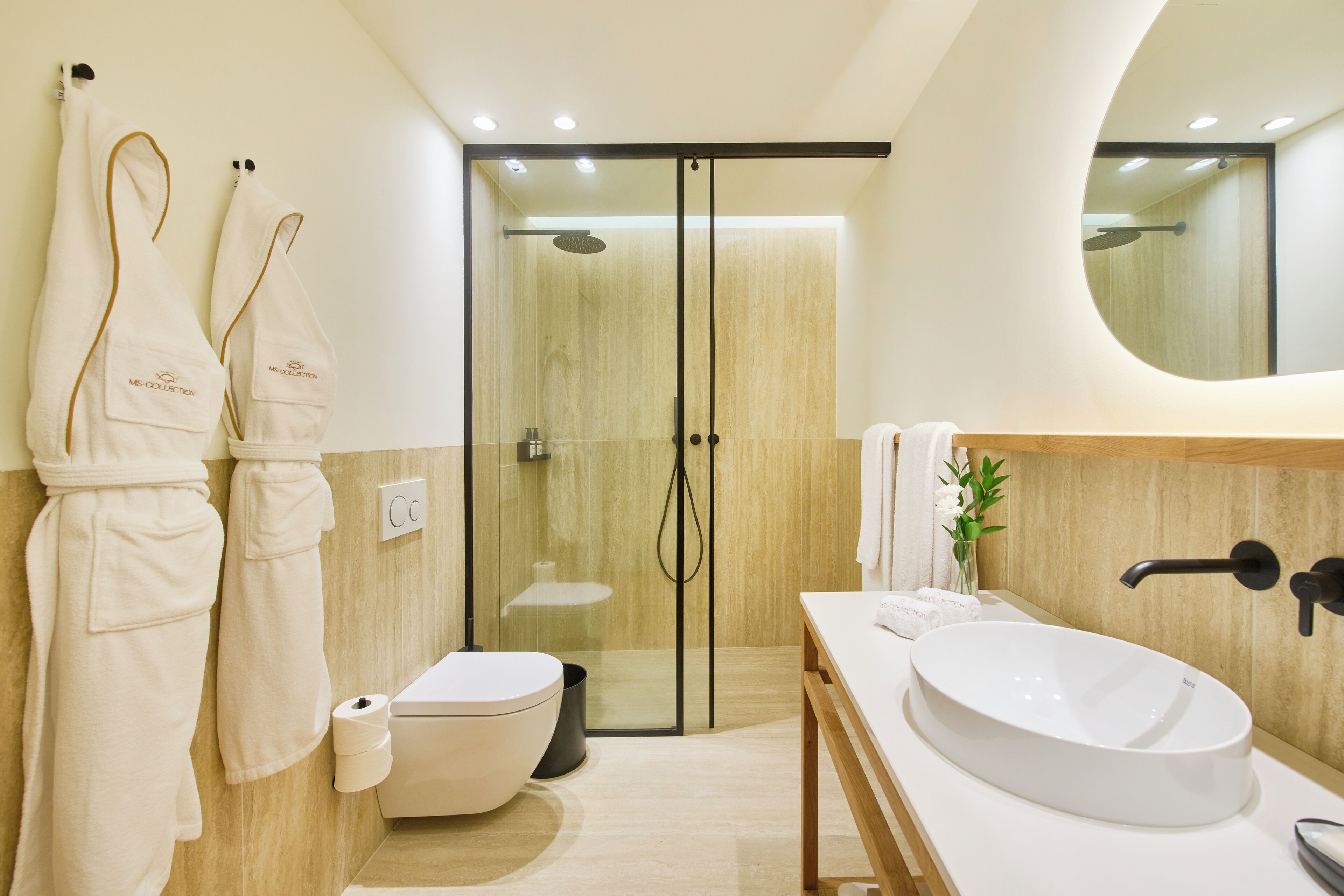 Un bagno moderno con uno specchio grande, un lavandino bianco e una cabina doccia in vetro.