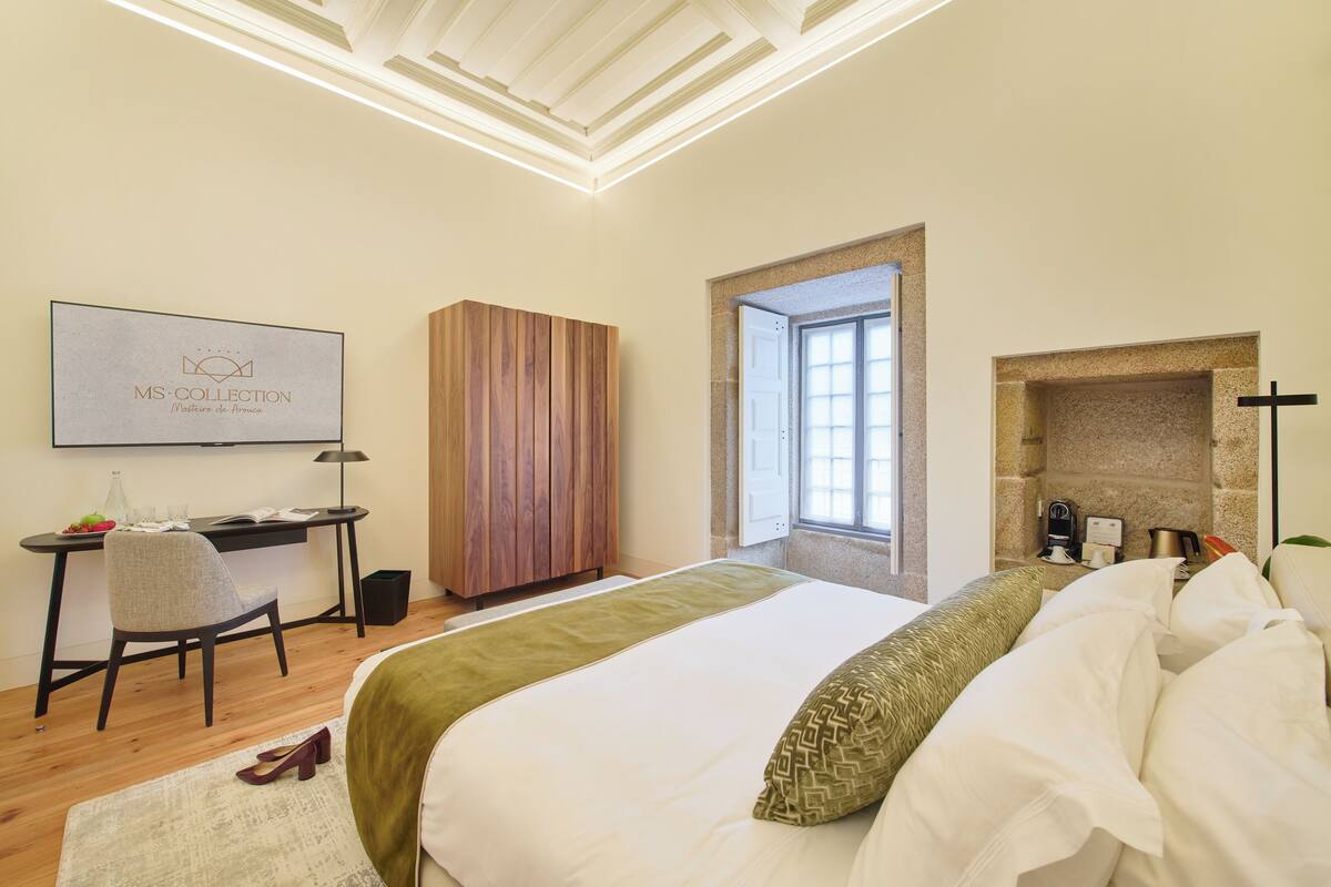 A bedroom with a bed, a desk, a chair, a wardrobe, and a fireplace.