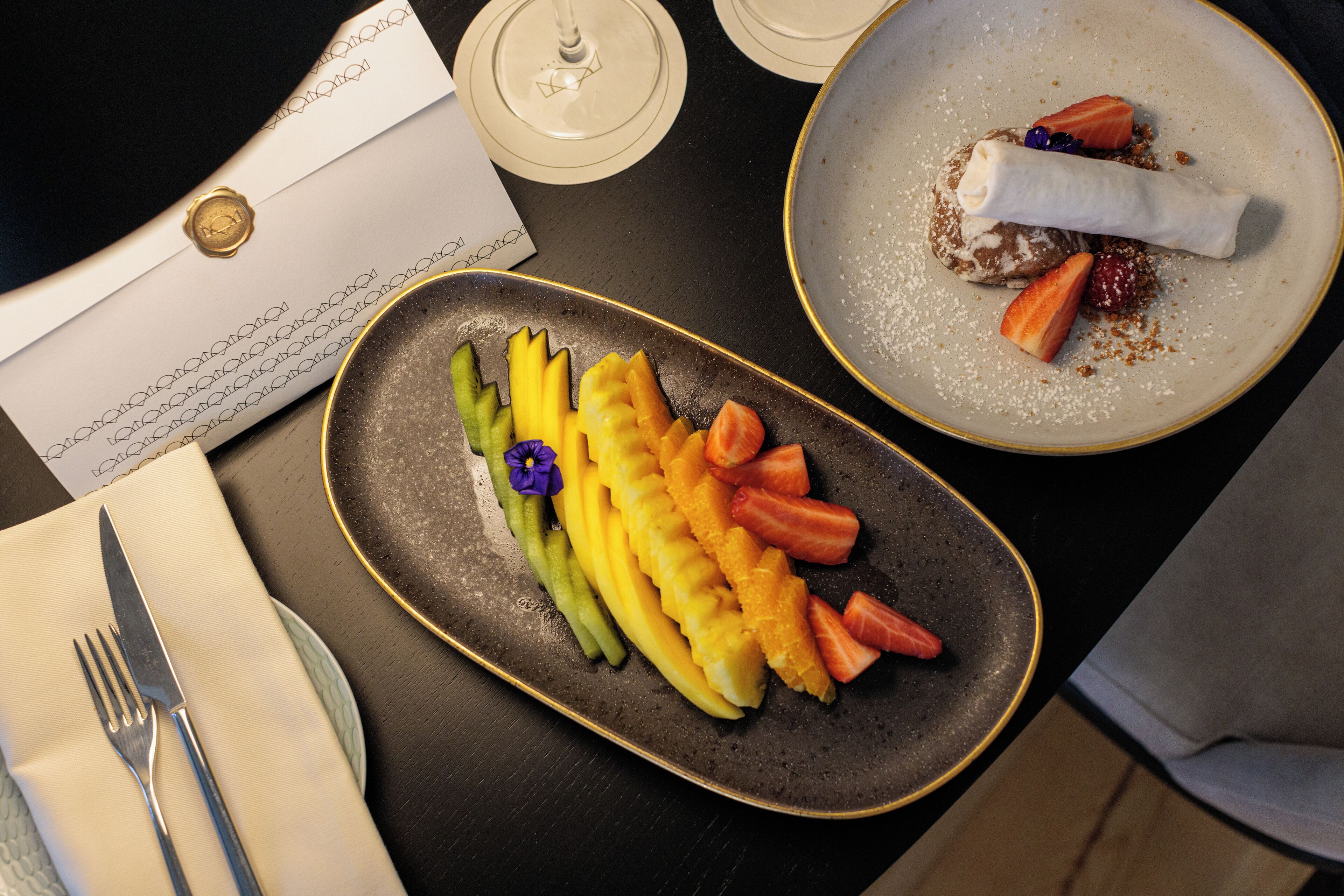 A dining table with a plate of fruit, a dessert, and a sealed envelope.