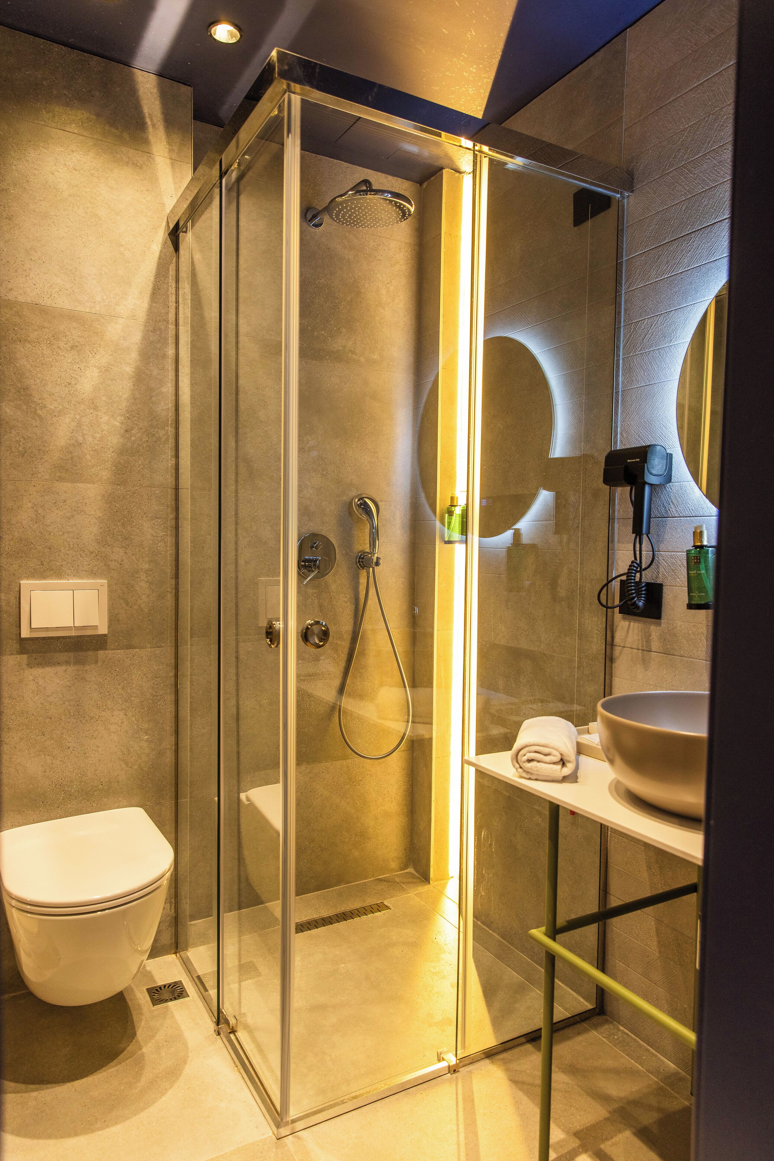 Un baño moderno con ducha de vidrio, inodoro y lavamanos con espejo.