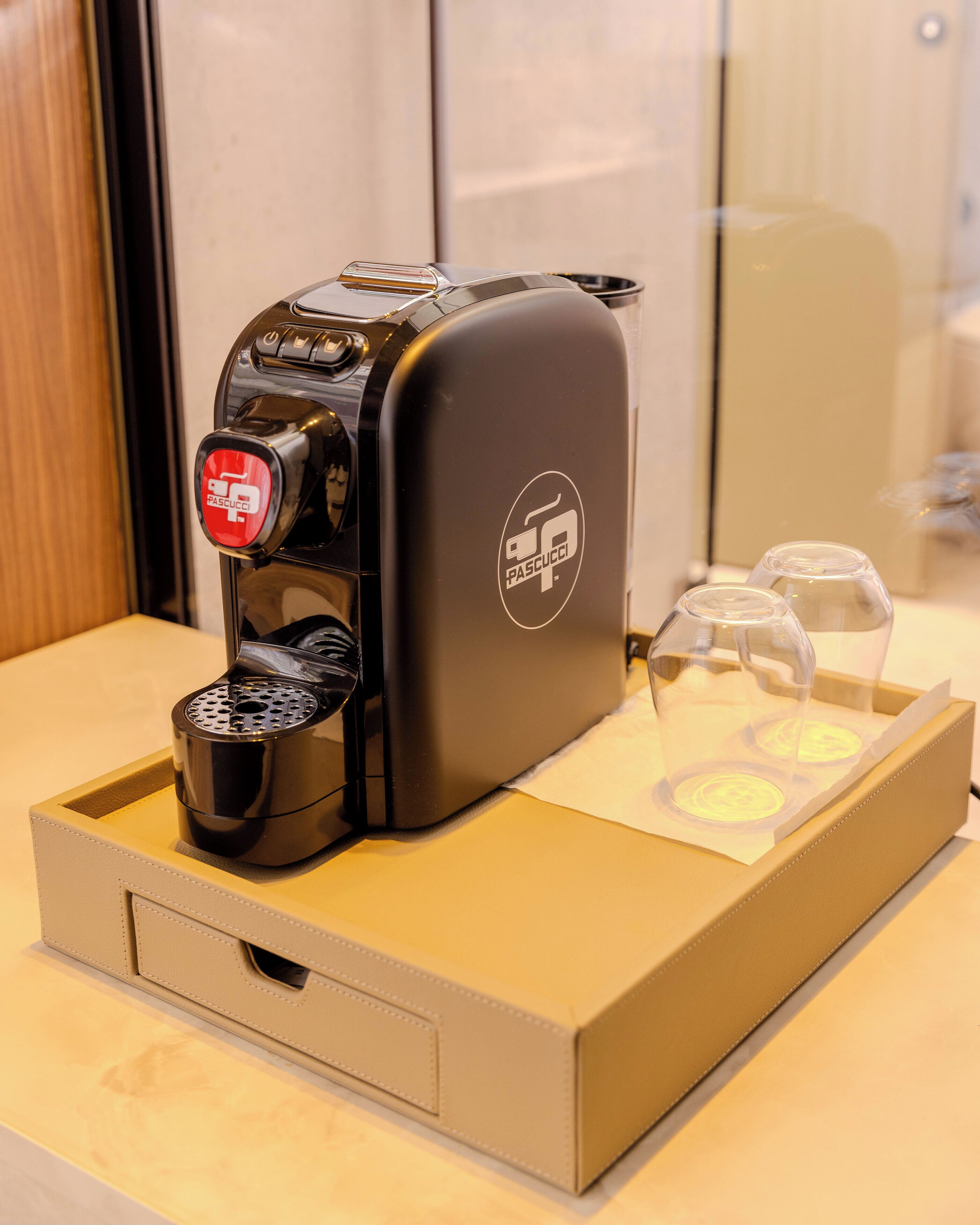 A coffee machine with a Pascucci logo, a cup of coffee, and two glasses on a tray.
