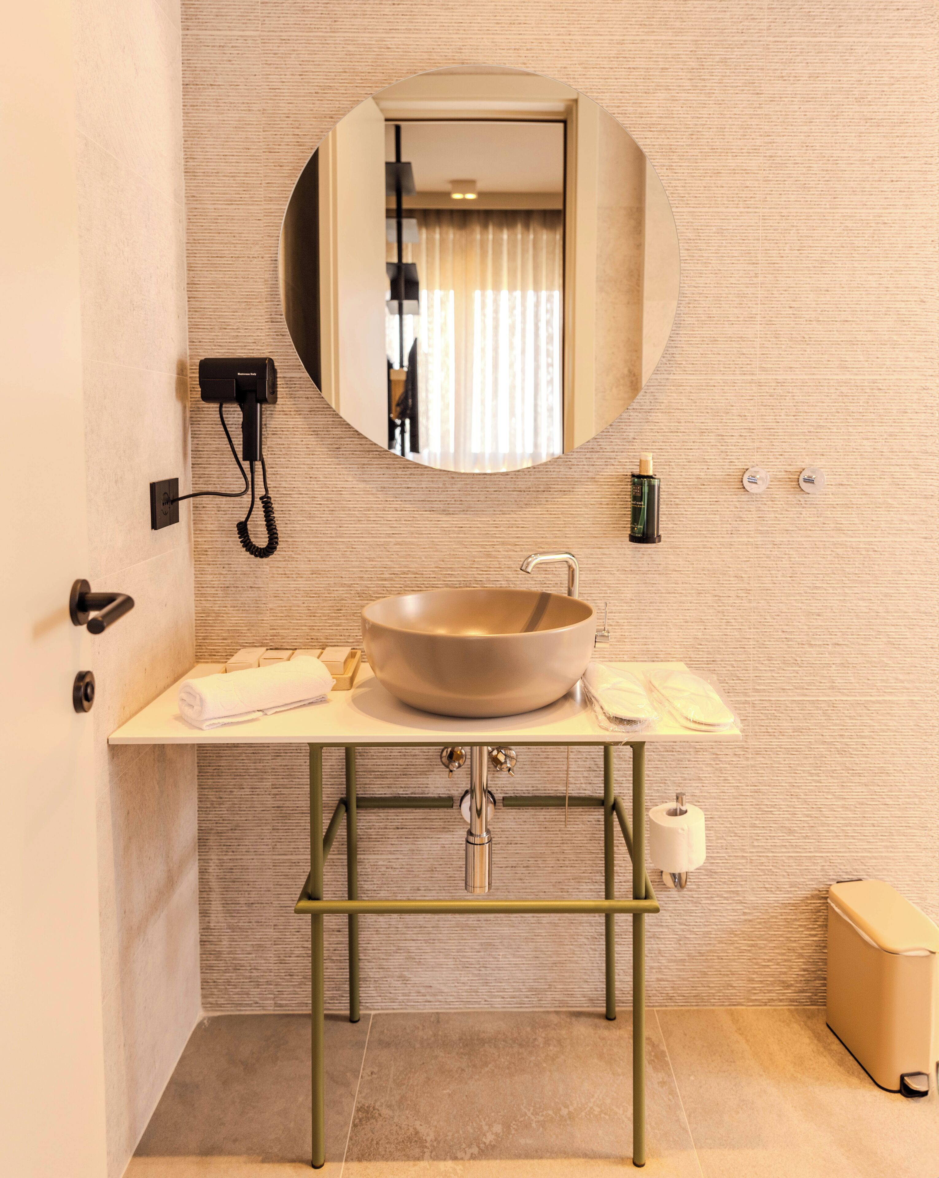 Un baño con un espejo redondo, un lavamanos color beige y una toalla sobre la encimera.
