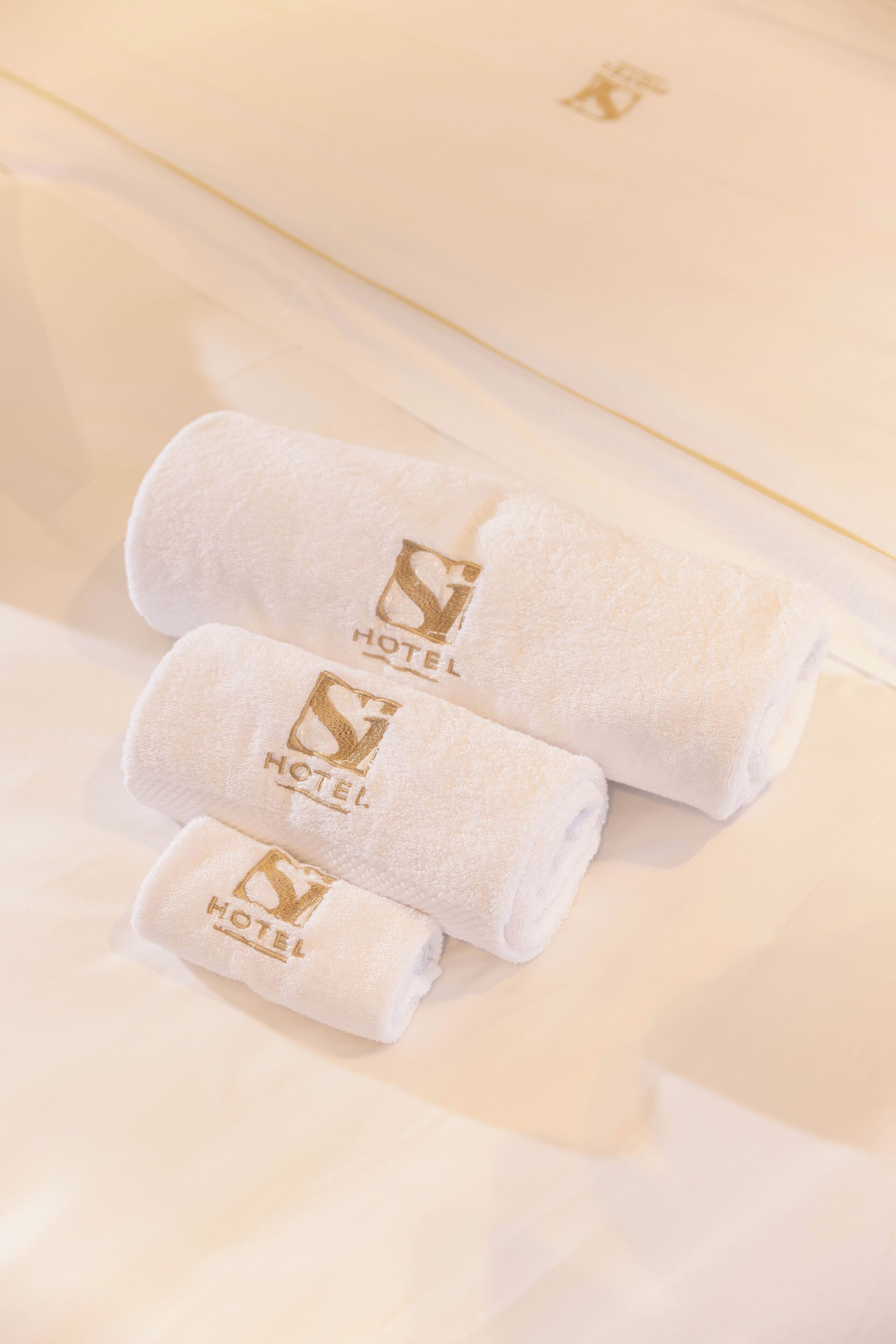 Drie netjes opgevouwen witte handdoeken met een hotel logo op een bed.