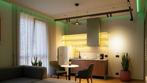Ein modernes Wohnzimmer mit einer Couch, einem Esstisch und Stühlen. Es gibt eine Küchenzeile mit einem Kühlschrank und einer Spüle.