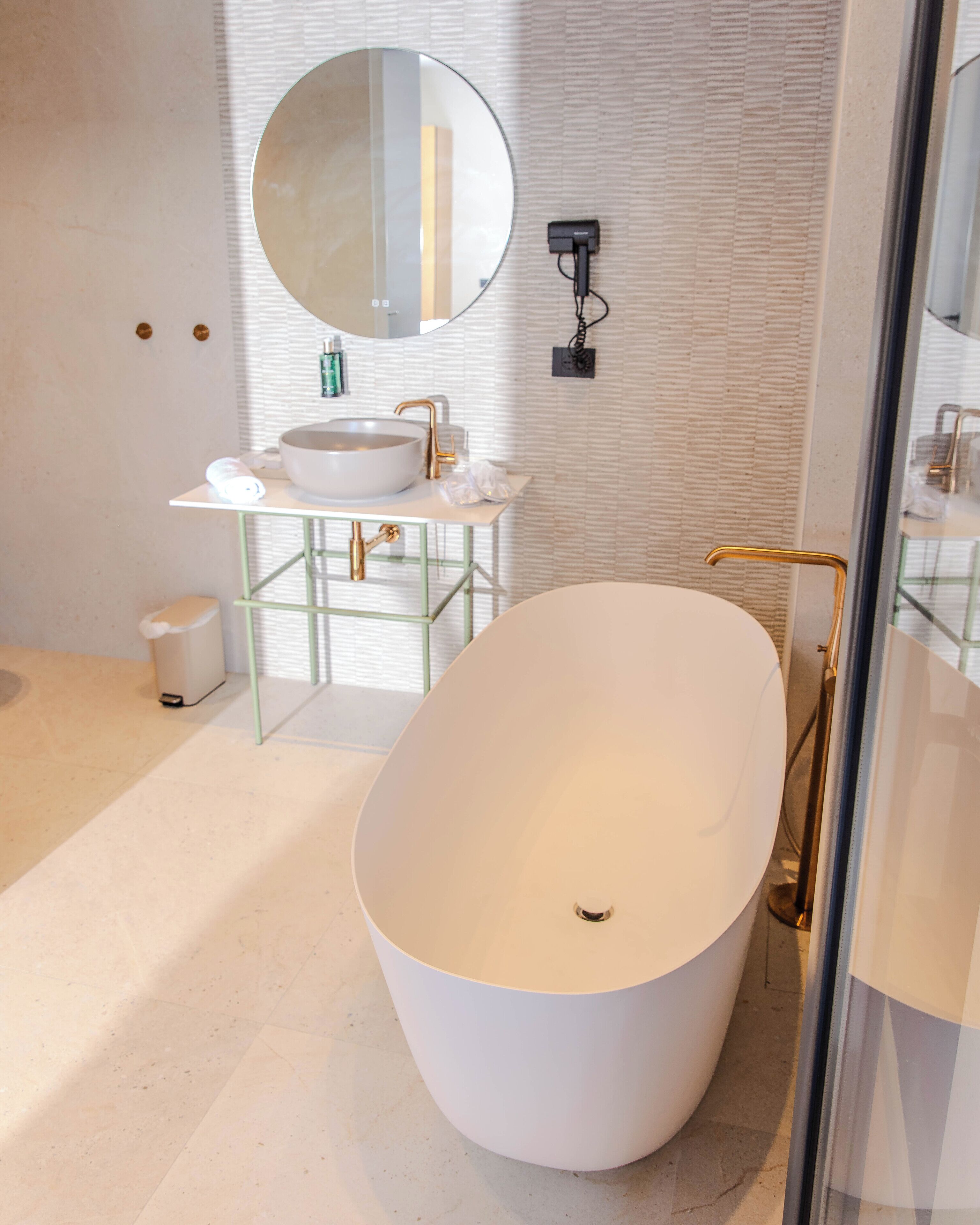 A modern bathroom with a freestanding bathtub, a round mirror, and a white sink with a gold faucet.