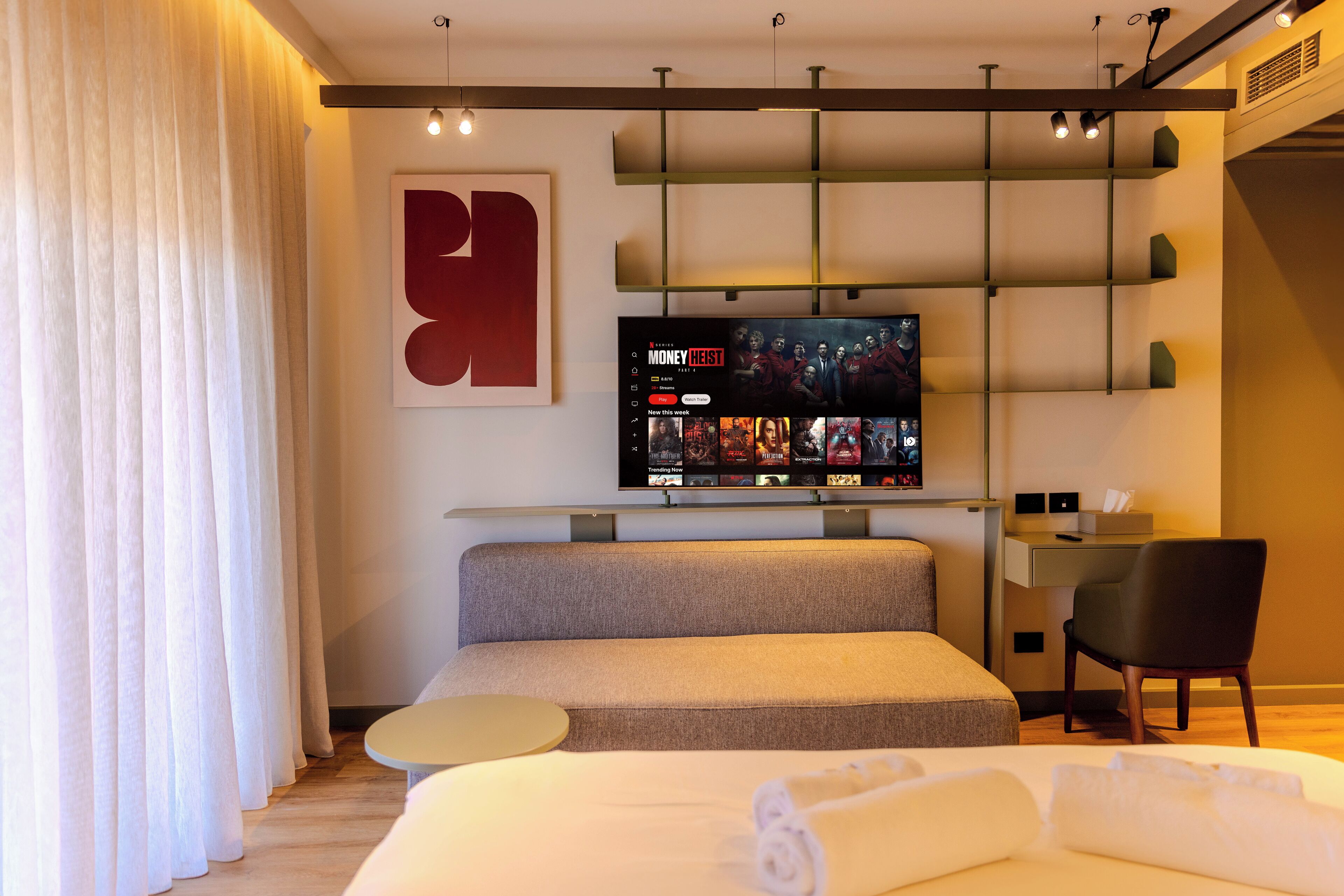 Une chambre d’hôtel moderne, dotée d’un grand lit, d’un bureau, d’une chaise, d’une télévision et d’une grande œuvre d’art abstraite accrochée au mur.