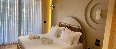 A modern hotel room with a large bed, neatly made with white linens and rolled towels.