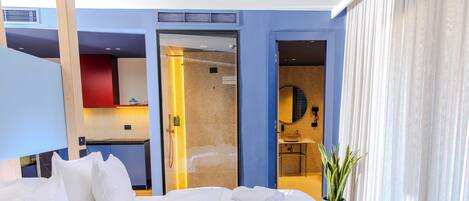 A modern hotel room with a large bed, a bathroom with a mirror, and a potted plant.