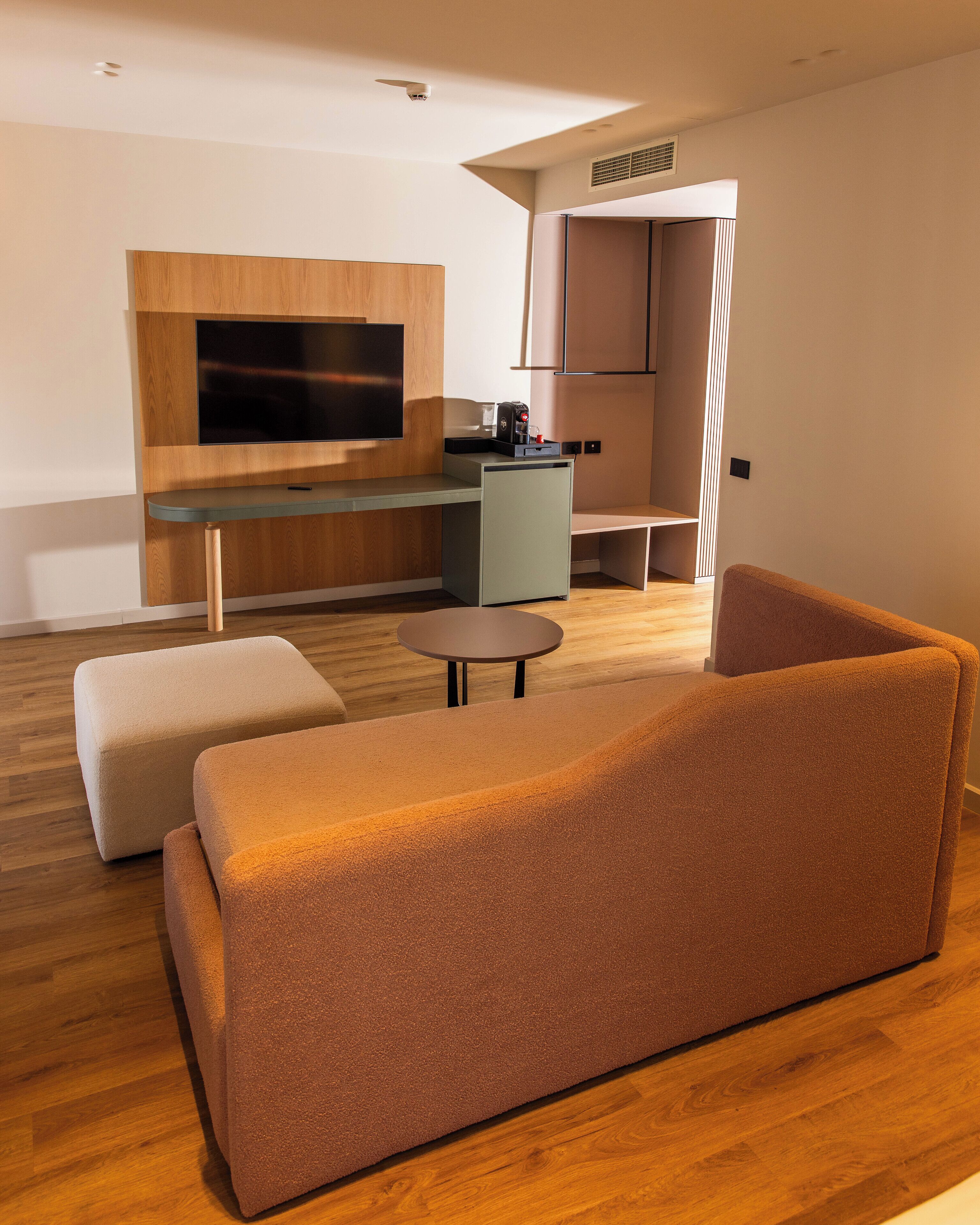 Een moderne woonkamer met een bank, poef, salontafel en een flatscreen televisie bevestigd aan een houten wand.