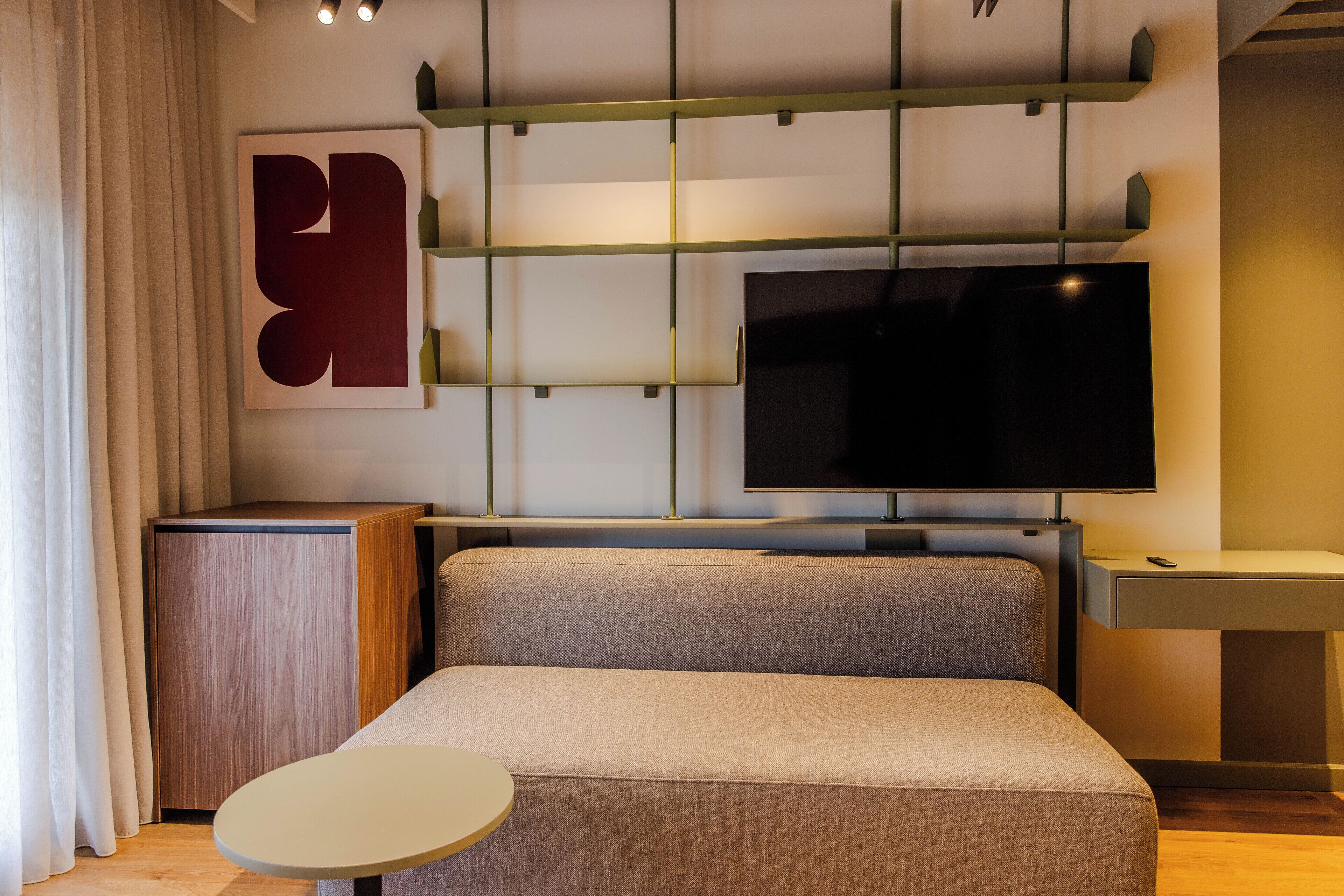 A modern living room with a sofa, a small round table, a TV mounted on the wall, and a wooden cabinet.