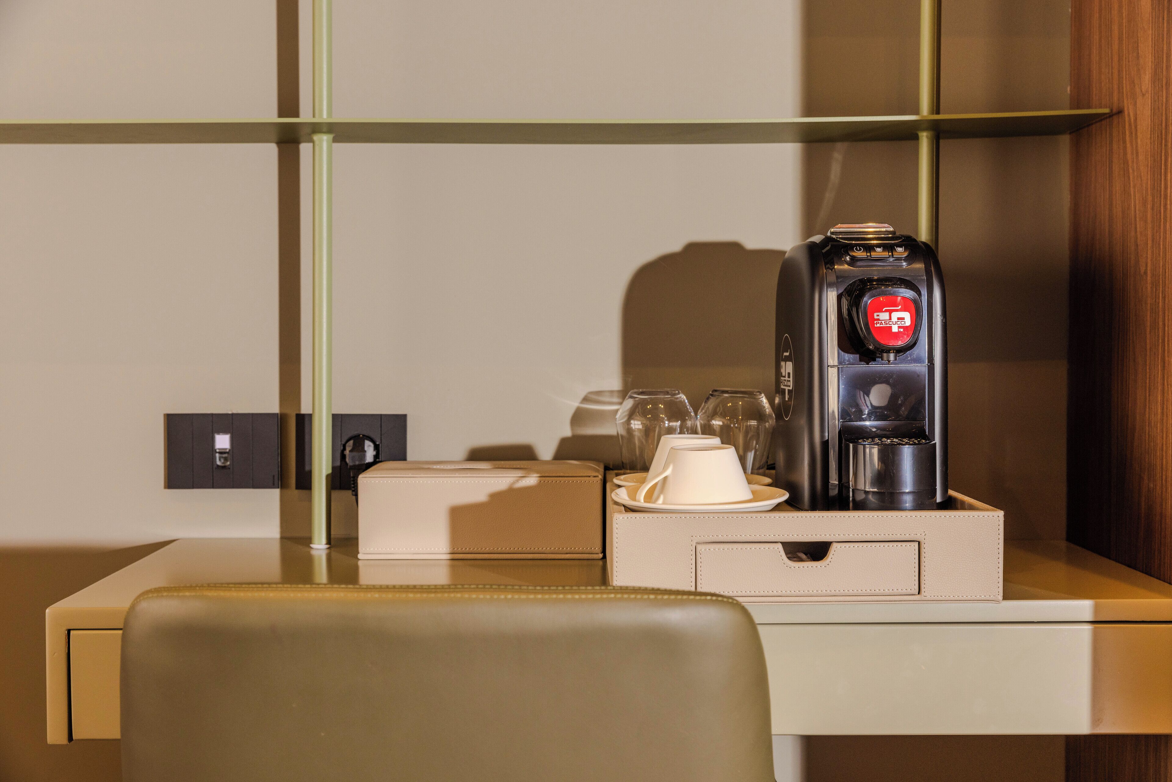 A hotel room with a desk, a coffee maker, a cup, and a glass set.