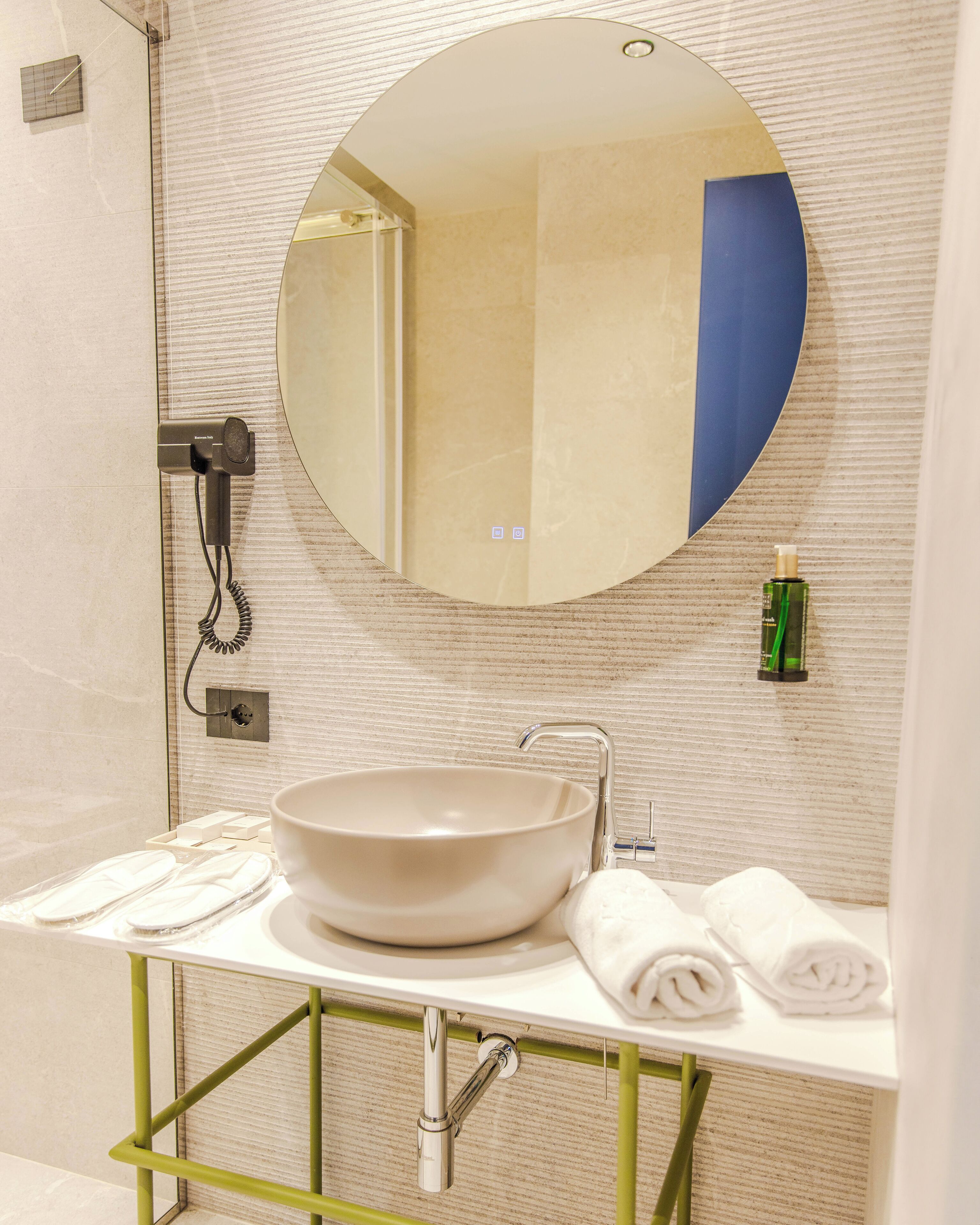 Une salle de bain avec un miroir rond, un lavabo, un porte-serviettes et un sèche-cheveux.