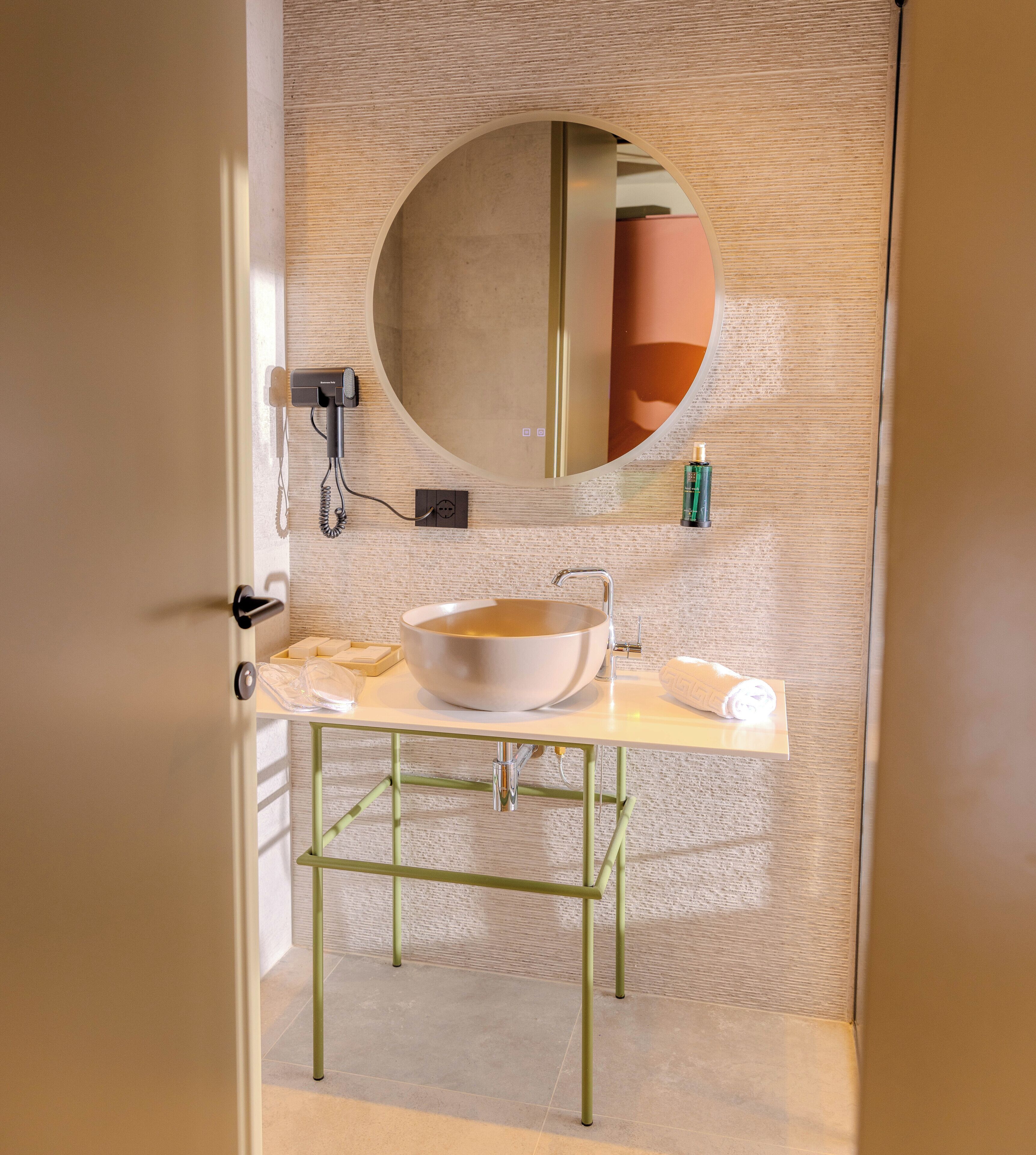 Un bagno con uno specchio tondo, un lavandino e un asciugamano sul ripiano.