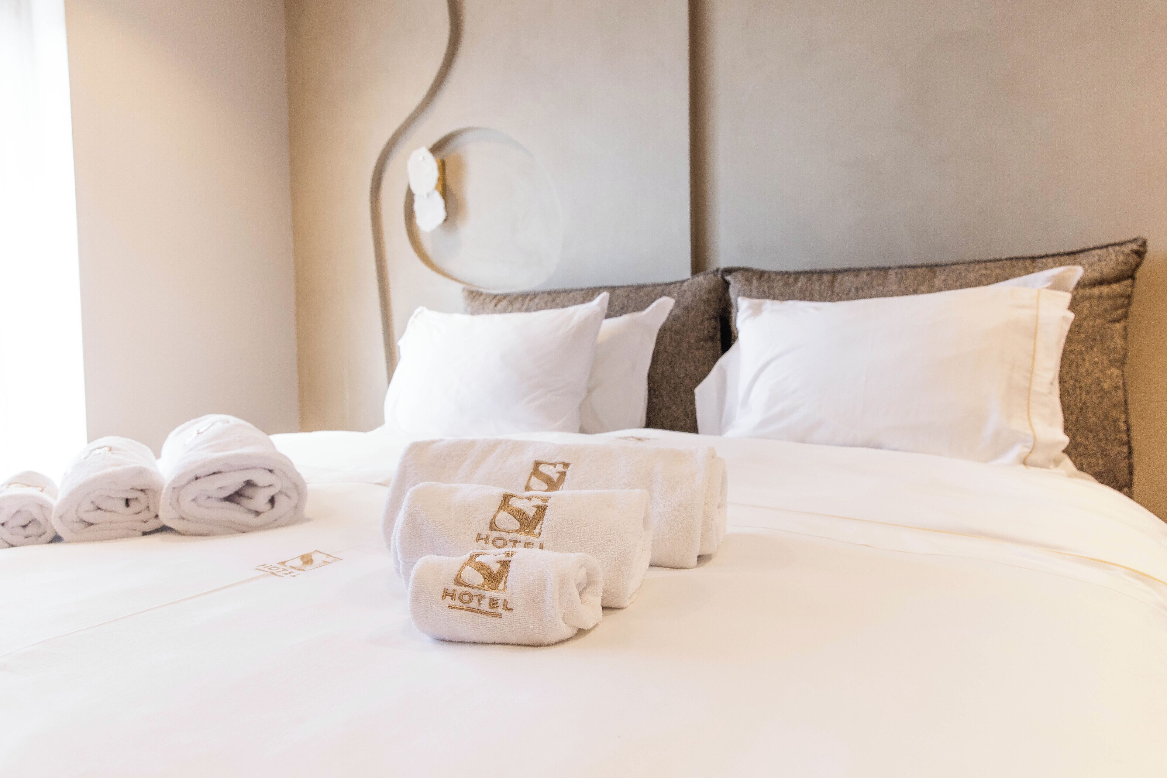 A neatly made bed with white linens and towels, a modern headboard, and a clean, minimalist design.