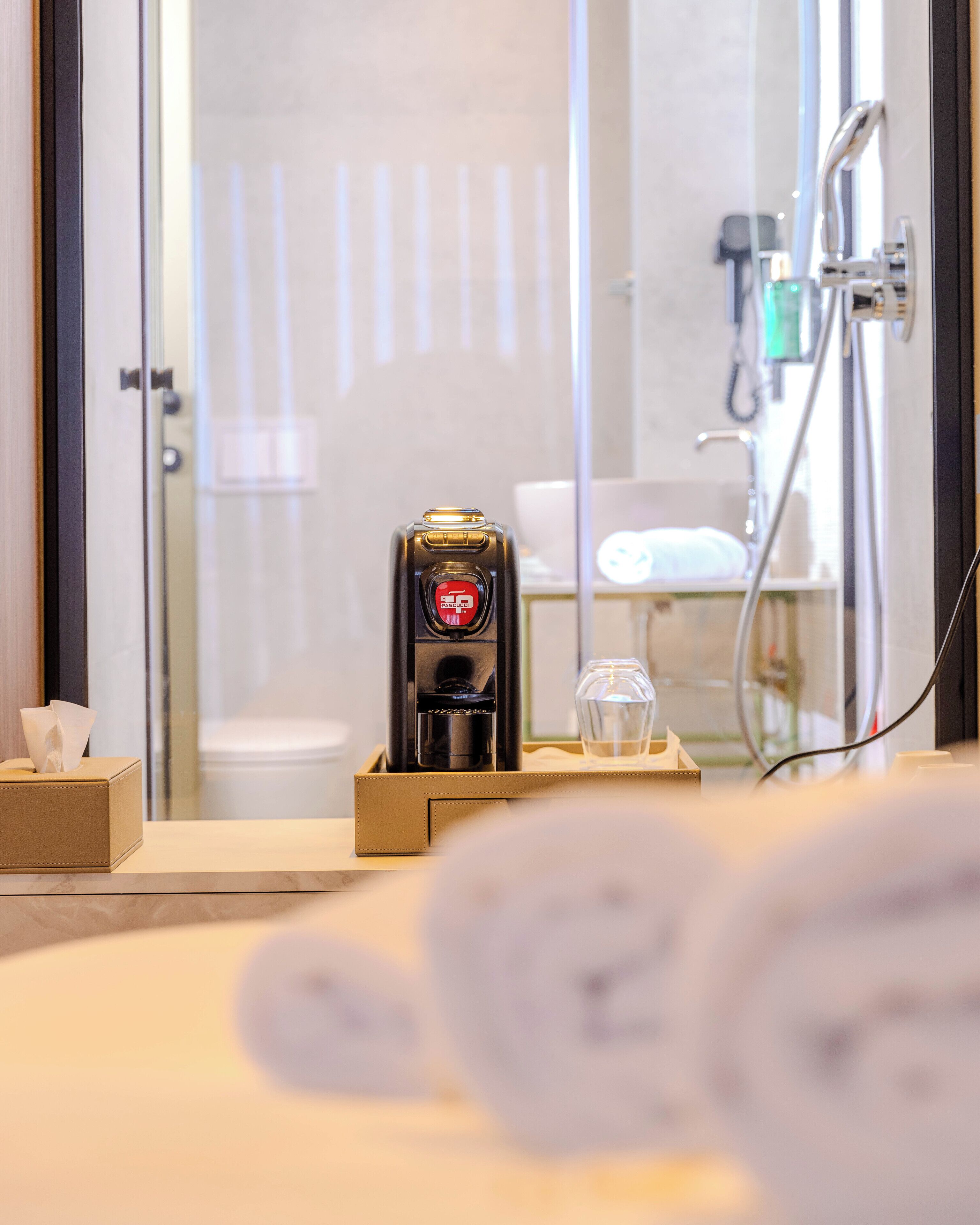 Een badkamer met een koffieapparaat, een glas water en handdoeken op het aanrecht.