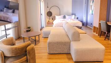 A modern hotel room with a large bed, a sofa, a TV, and a desk.