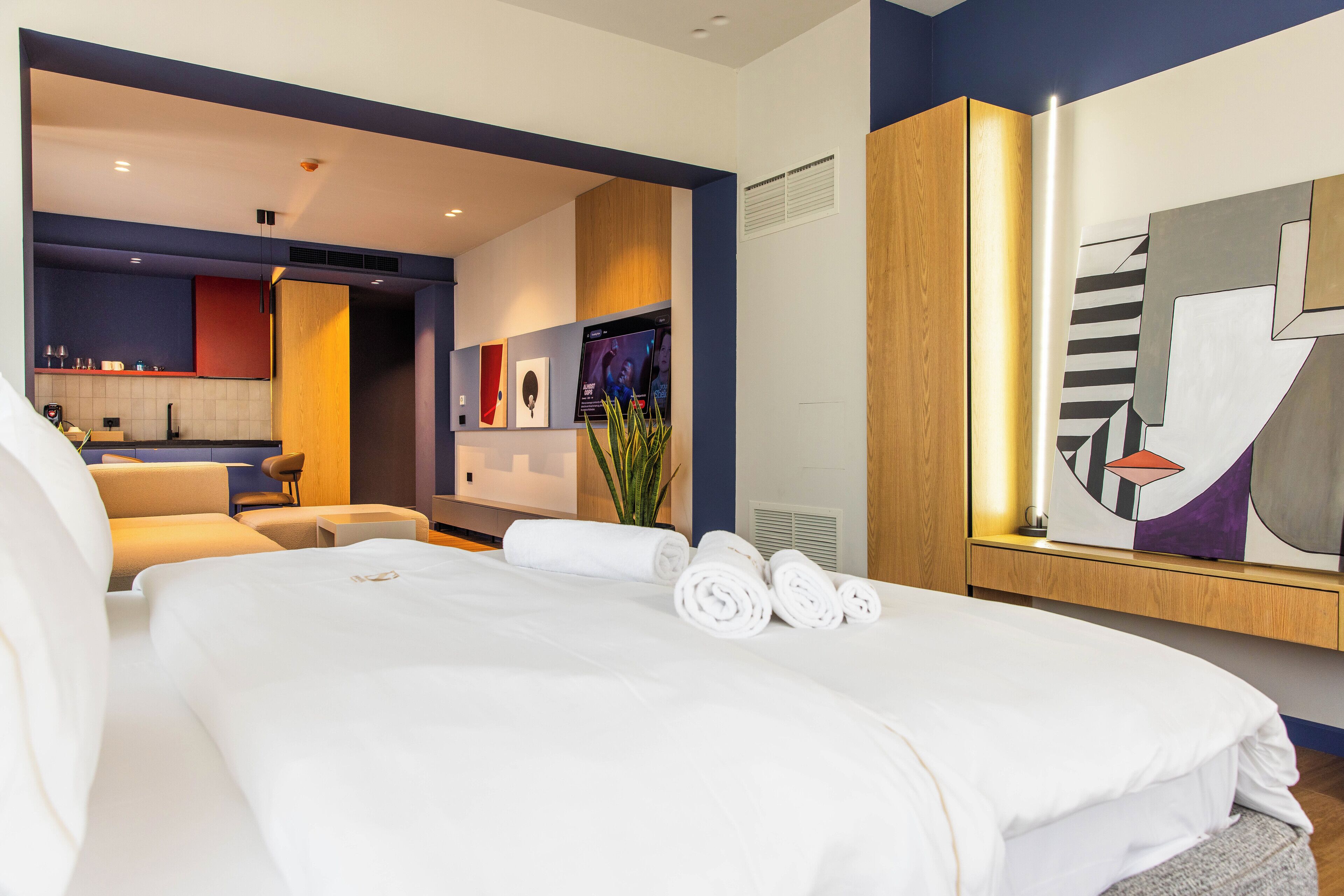Ein modernes Hotelzimmer mit einem großen Bett, einer Sitzecke mit Sofa und kleinem Tisch, einem Badezimmer mit Spiegel und Blick auf die Stadtlandschaft.