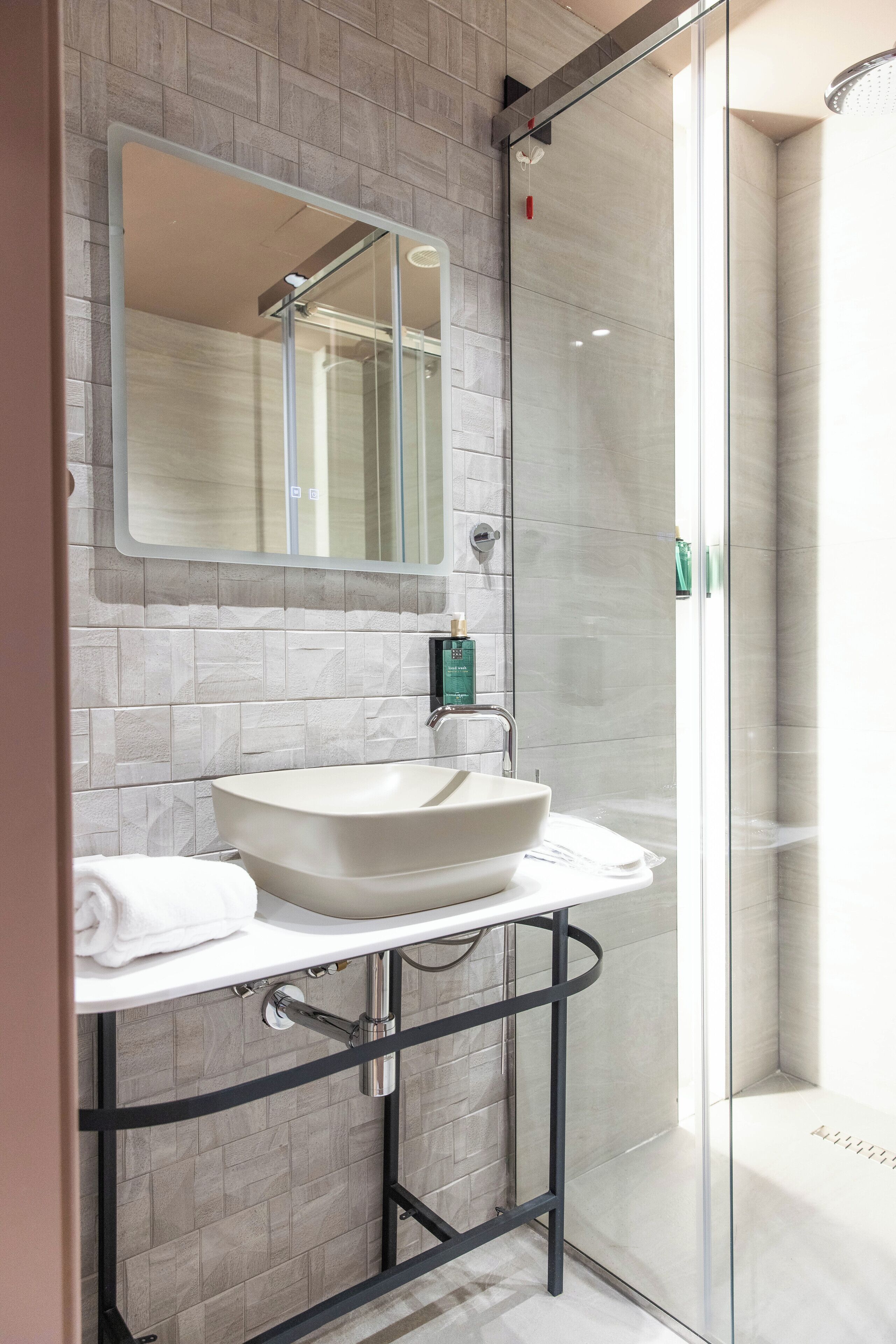 Une salle de bain moderne avec une douche à parois de verre, un lavabo blanc et un miroir au-dessus.