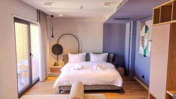 Habitación de hotel moderna con una cama grande, una mesa redonda, una silla y vistas a través de una puerta corrediza de cristal.