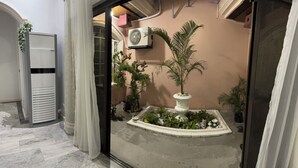 Een smalle gang met een kleine tuin met potplanten en een decoratieve boom.