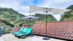 Une terrasse sur le toit, dotée d’un sol carrelé, de deux fauteuils de jardin verts et d’un grand parasol.