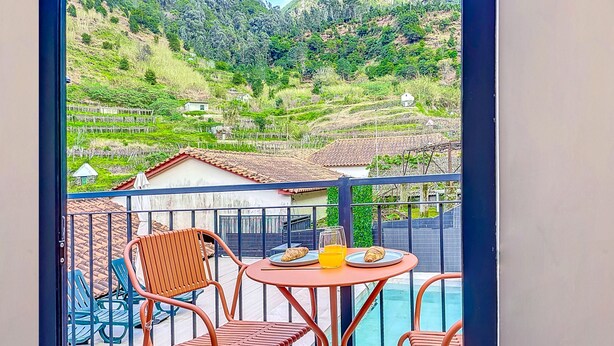 Un balcon avec une table et des chaises, donnant sur un paysage montagneux avec des champs en terrasses et des maisons.