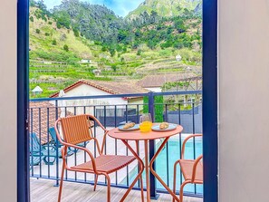 A balcony with a table and chairs, overlooking a mountainous landscape with terraced fields and houses.
