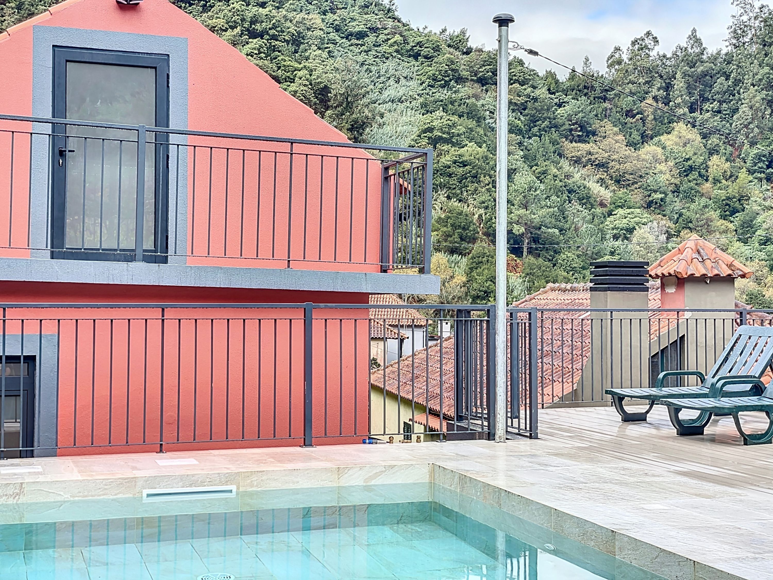 Un edificio de dos pisos con fachada roja y un balcón. Al frente, hay una piscina con un bordeado de azulejos.