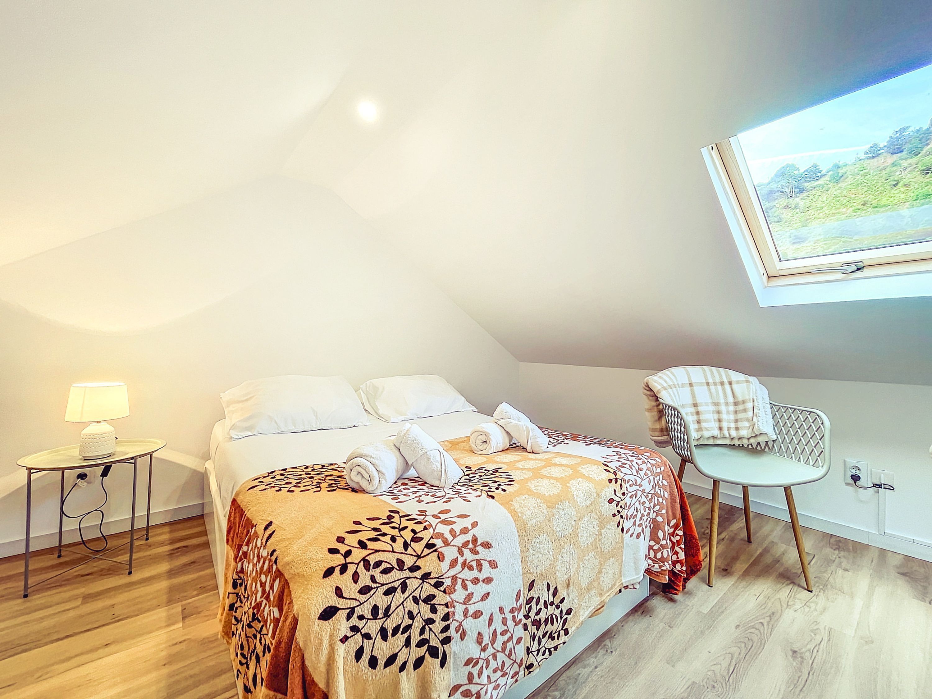 A bedroom with a bed, a bedside table with a lamp, a chair, and a painting on the wall.