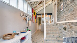 Une pièce avec un sol carrelé, un bureau blanc sur lequel se trouvent un bol et une paire de ciseaux, un banc et un mur en pierre.
