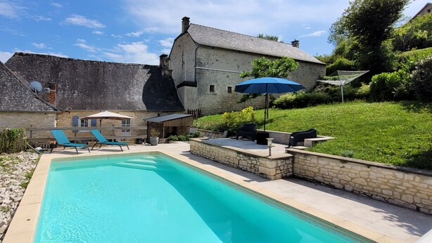 A swimming pool with lounge chairs and a patio area, surrounded by stone walls and a large stone building with a sloped roof. - In the heart of the village, house for 8 with pool (Coly)