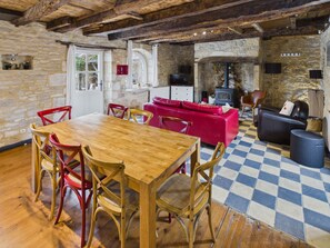 Interior rústico com mesa de jantar de madeira, cadeiras vermelhas, sofá vermelho e chão xadrez.