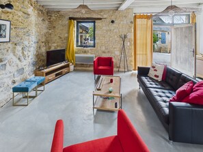 Un salon avec des murs en pierre, un canapé rouge, un canapé en cuir noir, une table basse en bois et un téléviseur.