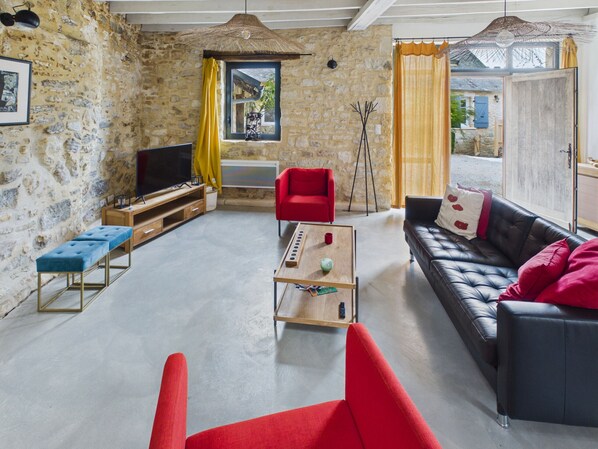 A living room with stone walls, a red sofa, a black leather sofa, a wooden coffee table, and a television.