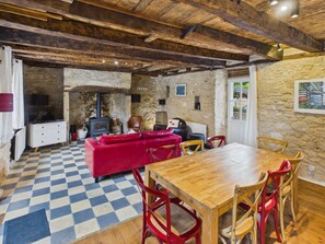 Un intérieur rustique avec un sol à carreaux, une table à manger en bois, des chaises rouges et en bois, un canapé rouge et des murs en pierre.